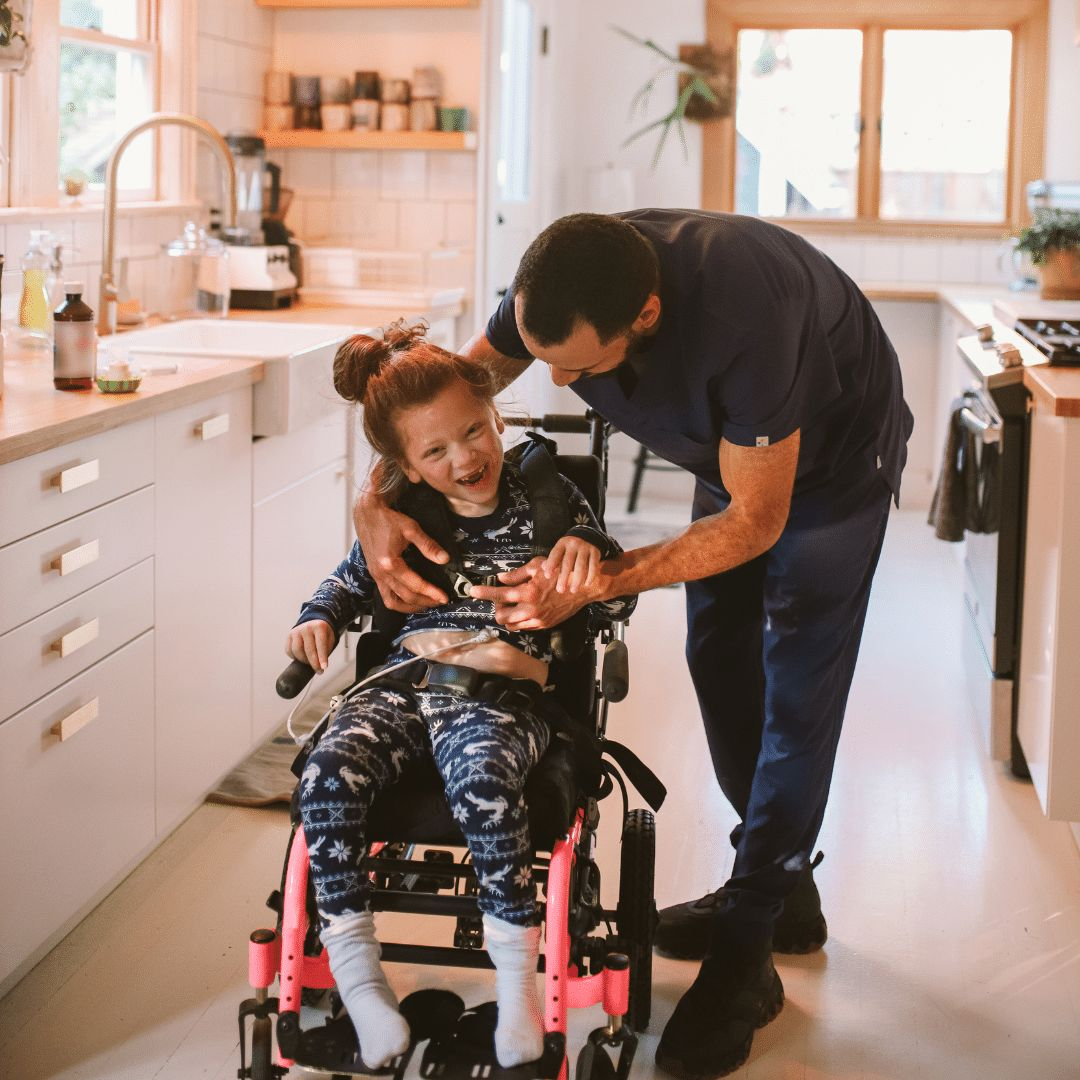 Support worker helping a smiling girl in a wheelchair at home in her kitchen